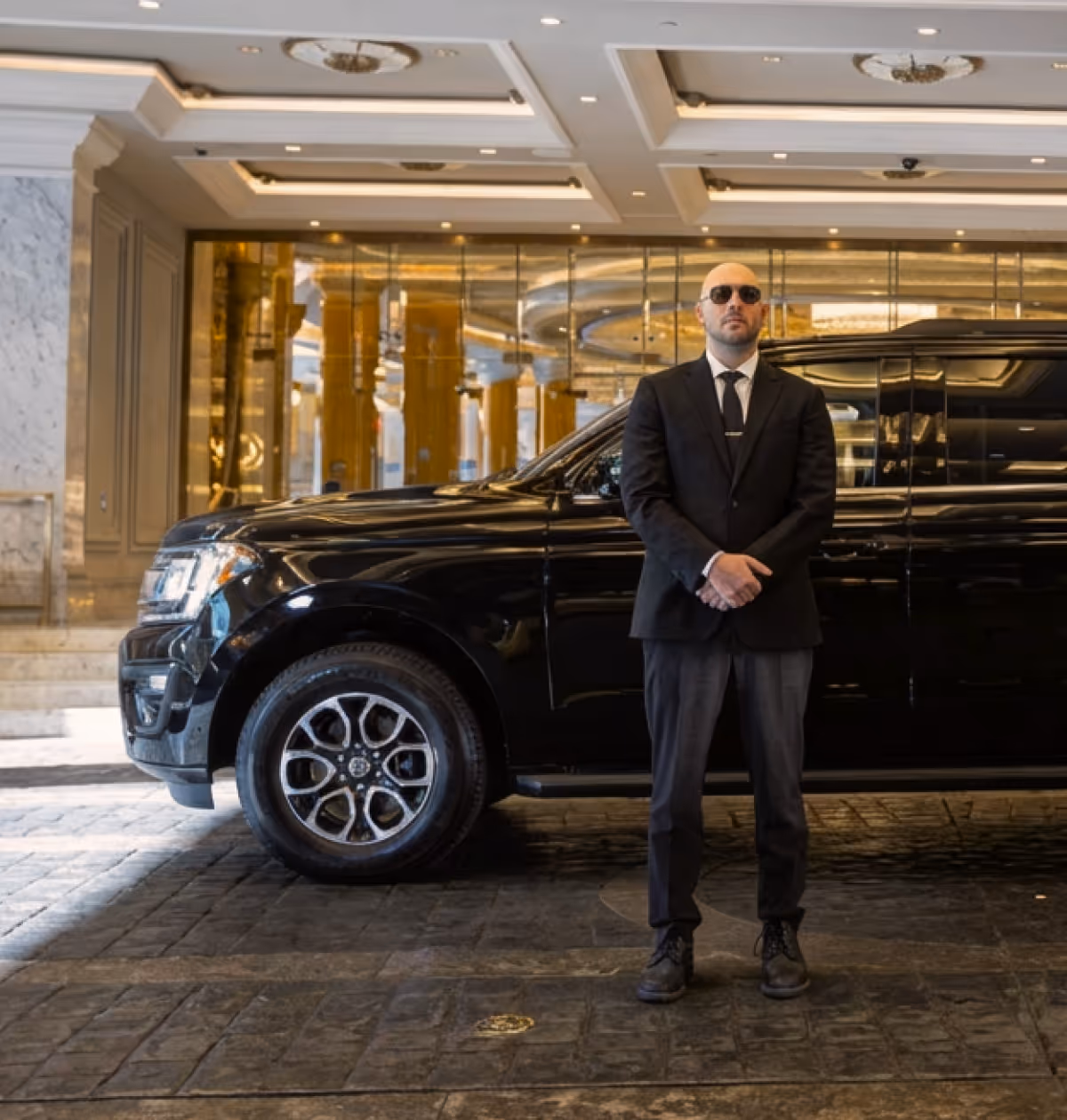 Private chauffeur standing by a black luxury car for hourly hire services.