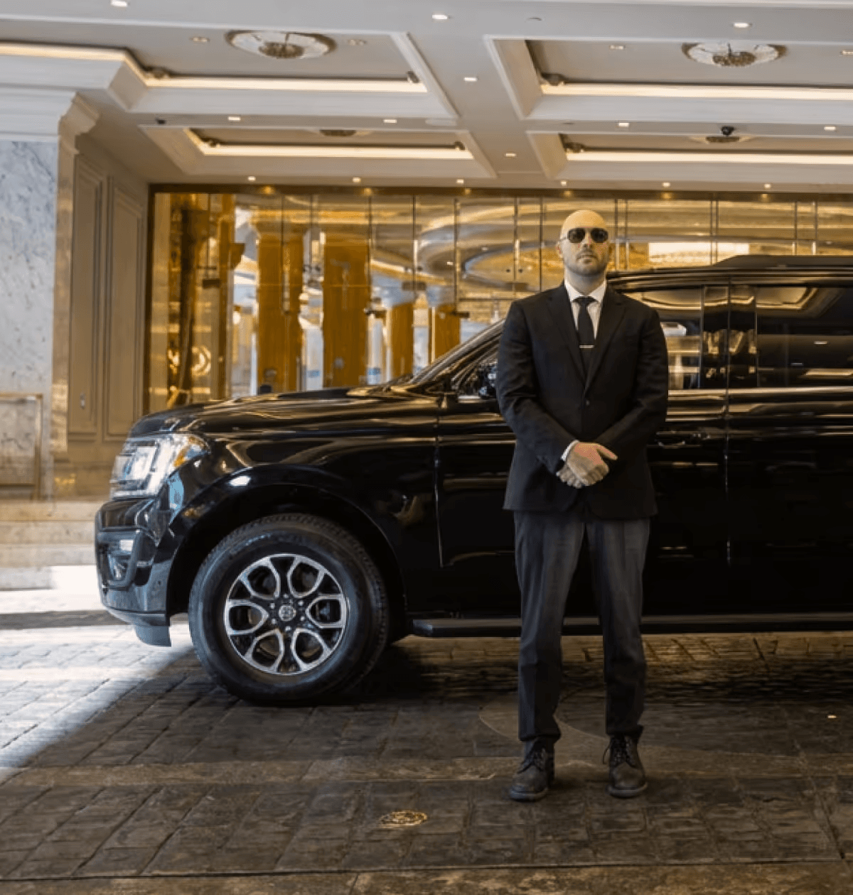 Private chauffeur standing by a black luxury car for hourly hire services.