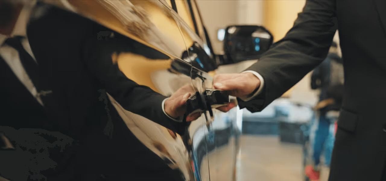 Chauffeur in a suit opening a black luxury vehicle door